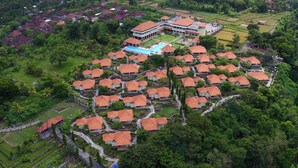 Vue aérienne d’un complexe hôtelier comprenant plusieurs bâtiments de style bungalow, une piscine centrale et une végétation luxuriante environnante.