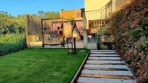 Un chemin mène à un bâtiment à la façade jaune, entouré d’une pelouse bien entretenue et d’un mur de pierres.