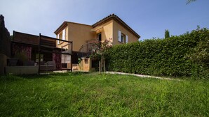 Une maison à deux étages avec un balcon, un jardin bien entretenu et un ciel d’un bleu éclatant.