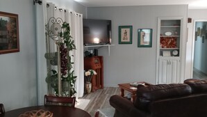 A living room with a brown leather sofa, a dining table with chairs, a TV mounted on the wall, and a bookshelf. - Cozy Hideaway in Town (Springdale)