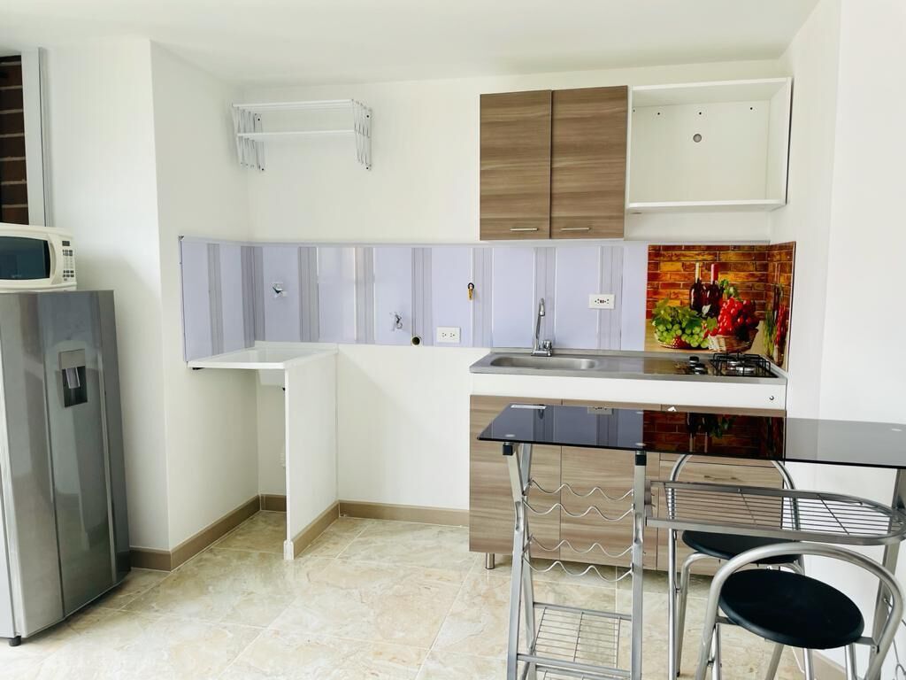 Cocina compacta con microondas, refrigerador y un pequeño comedor con mesa y sillas.