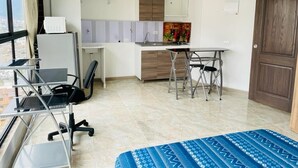Une chambre d’hôtel de taille réduite, comprenant un lit, un bureau, une chaise, une petite kitchenette et une fenêtre donnant sur la ville.