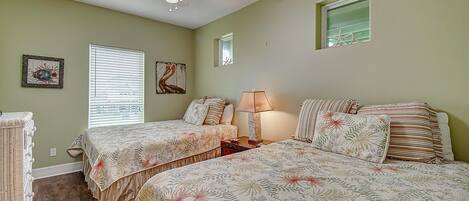 Makuuhuoneessa on kaksi sänkyä, kattotuuletin, ikkuna, jossa on sälekaihtimet, ja seinätaidetta.