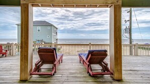 A wooden deck with two lounge chairs facing the ocean, a covered area, and a house in the background. - Sea Esta- Front Row Views-4 bedroom 3-1/2 bath home, sleeps 12 guests. (Port Bolivar)