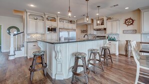 A spacious kitchen with white cabinetry, a large island with bar stools, and pendant lighting. - Sea Esta- Front Row Views-4 bedroom 3-1/2 bath home, sleeps 12 guests. (Port Bolivar)