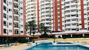 A multi-story hotel with a swimming pool, palm trees, and a yellow and white color scheme. - Bright apartment steps from Praia da Rocha, one of Portugal’s finest beaches. Access to a large pool, promenade, restaurants and cafés. Sleeps 5. Self check-in via lockbox. (Portimão)