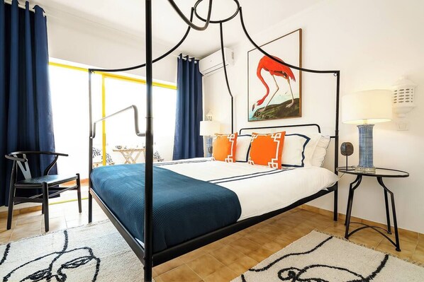 Ein Himmelbett mit blauer und weißer Bettdecke, orangefarbenen Kissen und einem Flamingo-Gemälde an der Wand.