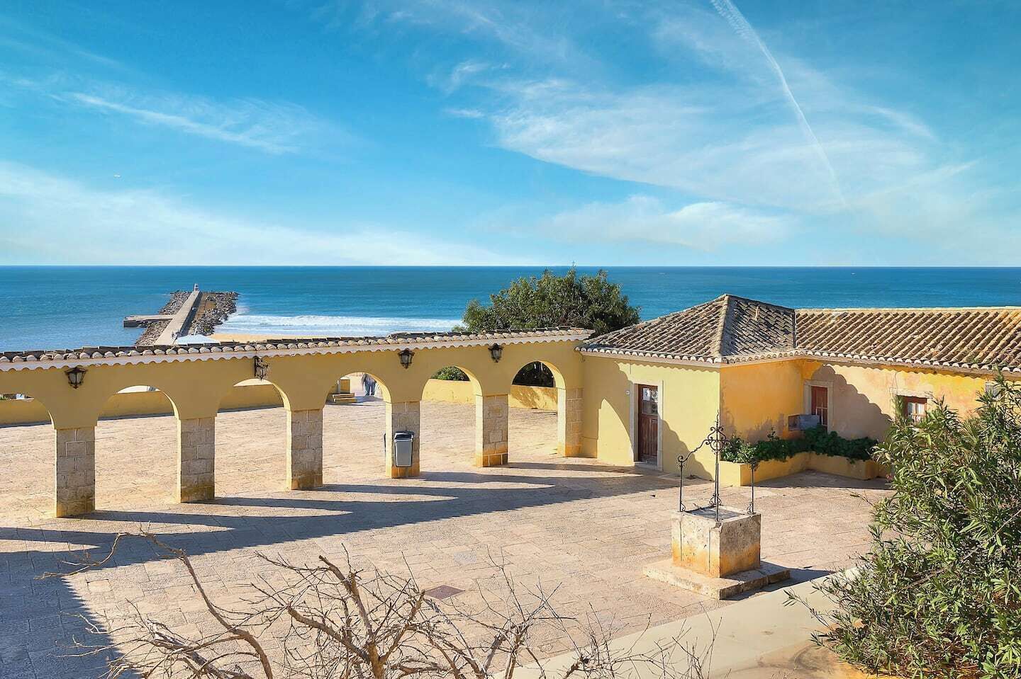 A coastal building with a tiled roof, a stone archway, and a view of the sea.