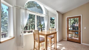 A dining area with a table and chairs, a large window with curtains, and a door with a glass panel.