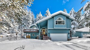 A two-story house with a garage, surrounded by snow-covered trees.