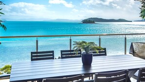 A dining area with a table and chairs, overlooking a turquoise sea with distant islands.