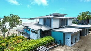 A modern coastal house with a large deck overlooking the sea, a covered outdoor area, and a small garden.