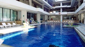 A large indoor swimming pool with multiple levels of balconies and lounge chairs around the pool area. - Palace In Moon Beach (Onna)