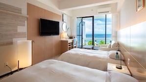A hotel room with two beds, a TV, a desk with a chair, a large window with a view of the sea, and an air conditioning unit. - Palace In Moon Beach (Onna)