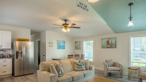 A spacious living area with a sofa, coffee table, and a ceiling fan. There is a kitchen area with a refrigerator and a dining table. - Pet Friendly Linens Included Rehoboth Beach House Parking Mini Golf (Rehoboth Beach)