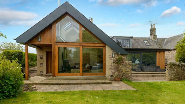 A modern house with a large glass front, a stone exterior, and a sloped roof. - Fidra Cottage - Stunning Place to Stay! (North Berwick)