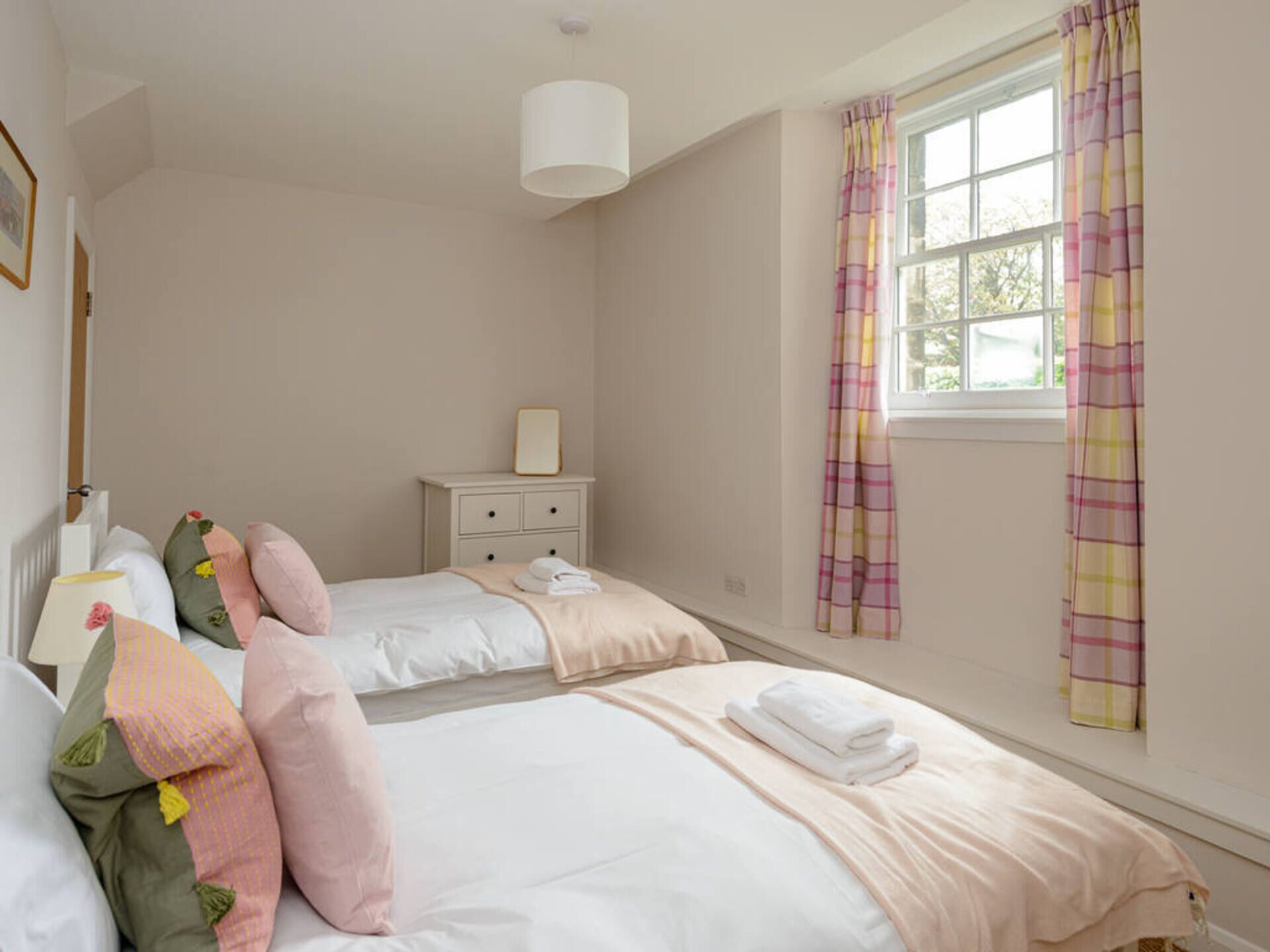 Een slaapkamer met twee bedden, een nachtkastje met lamp, een raam met gordijnen en een wandlamp.
