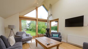 A spacious living room with a large wooden coffee table, grey sofas, and a fireplace. - Fidra Cottage - Stunning Place to Stay! (North Berwick)