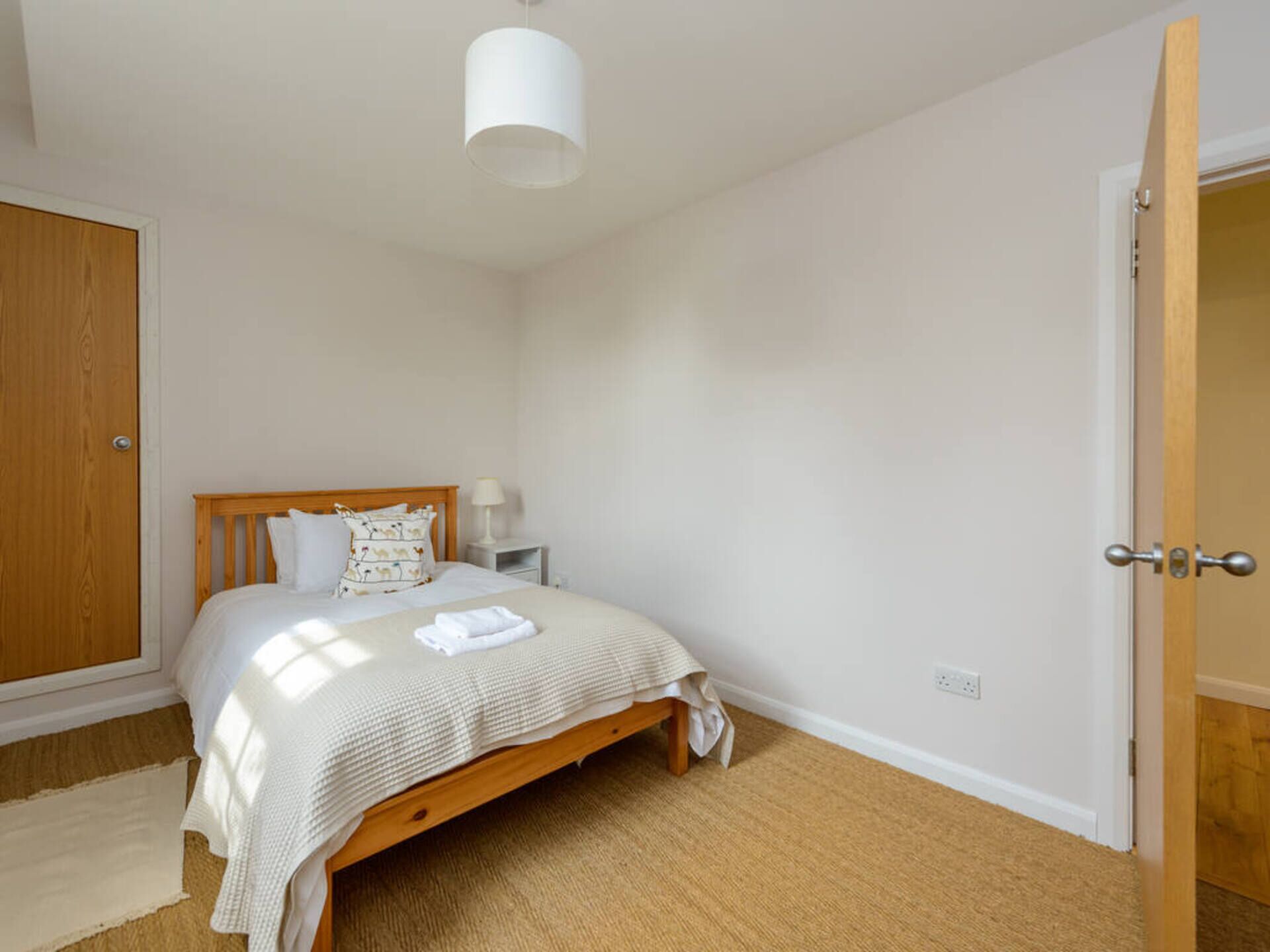 A bedroom with a wooden bed, a nightstand, a lamp, and a door.