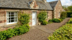 A stone house with a tiled roof, a white door, and a gravel driveway. - Fidra Cottage - Stunning Place to Stay! (North Berwick)