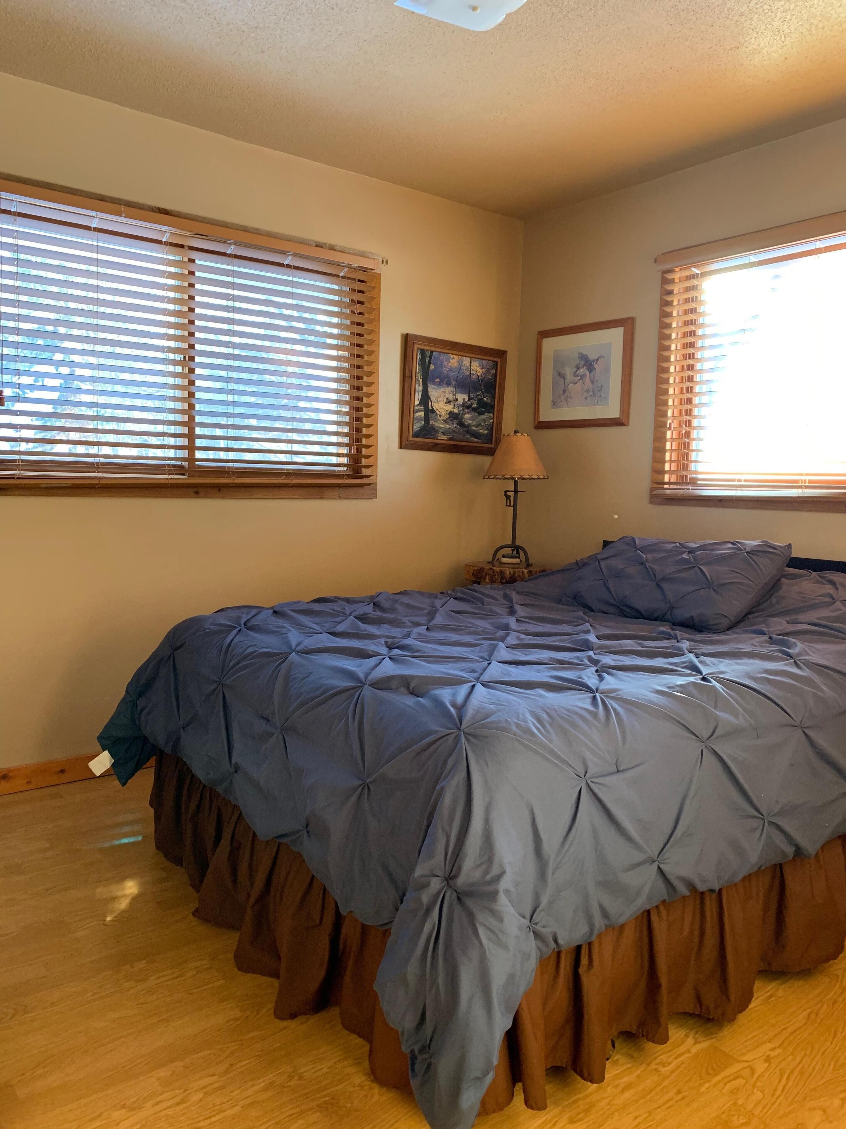 A bedroom with a large bed, wooden blinds, a painting, and a lamp.