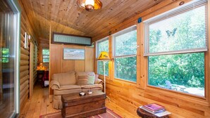 Interior acogedor de una cabaña con piso de madera, un sofá, una mesa y ventanas amplias con vistas al bosque.