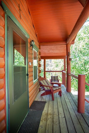 A log cabin with a covered porch, two chairs, and a bench.