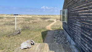 Una construcción de madera con puerta de cristal y un camino que lleva a un paisaje arenoso.