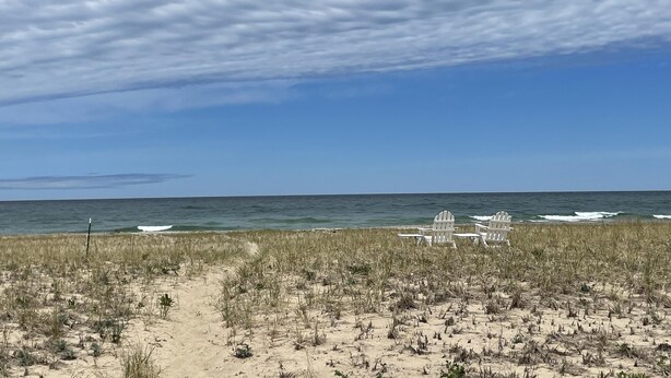 Una playa con sillas blancas y una estructura pequeña, posiblemente un pabellón, a lo lejos.