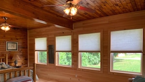 A wooden cabin interior with a wooden floor, a ceiling fan, and a bed with a blanket. - Paul's Place - Two blocks from beaches in the heart of Grand Marais (Grand Marais)