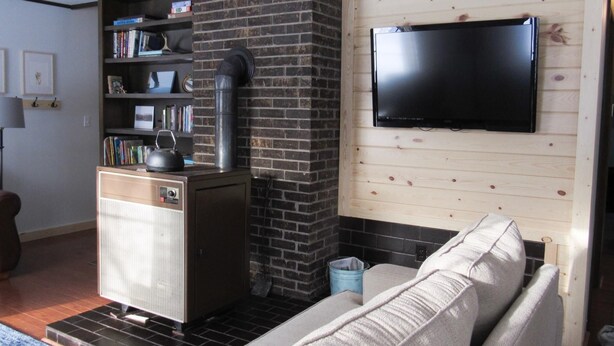 A living room with a brick fireplace, a television mounted on the wall, and a sofa. - Aspen House - Stunning 4 Bedroom A-Frame (Grand Marais)