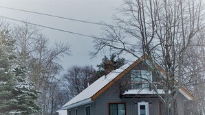 A two-story house with a sloped roof, a front porch, and a garage. - Aspen House - Stunning 4 Bedroom A-Frame (Grand Marais)