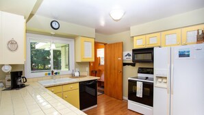 A compact kitchen with yellow cabinets, a white refrigerator, a microwave, and a dishwasher. - Firefly House - Comforts of home across from beach/campground (Grand Marais)