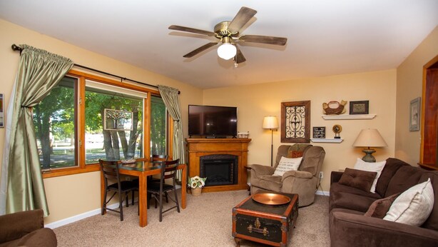 A living room with a fireplace, a television, a ceiling fan, and a dining area with a table and chairs. - Firefly House - Comforts of home across from beach/campground (Grand Marais)