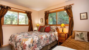 A bedroom with a large bed, two bedside tables, a nightstand, and a window with curtains. - Firefly House - Comforts of home across from beach/campground (Grand Marais)