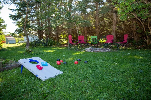 A backyard with a lawn game setup, including a white board with holes and balls, and several folding chairs. - Firefly House - Comforts of home across from beach/campground (Grand Marais)