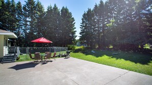 A patio with a table and chairs, a red umbrella, and a view of a forested area. - Firefly House - Comforts of home across from beach/campground (Grand Marais)
