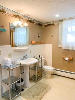 A bathroom with a sink, toilet, and mirror. There is a towel rack and a shelf with toiletries.