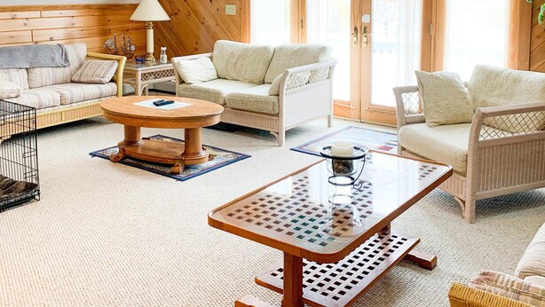Una habitación acogedora y bien iluminada, con paredes de madera y techo inclinado, que incluye un conjunto de sofás, una mesa de centro y una bandera colgante de Spartan's Will.