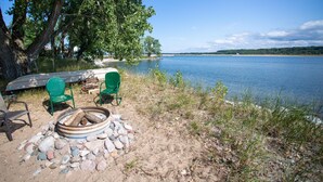 Un cadre idyllique au bord du lac, avec un foyer, deux chaises vertes et un canoë.