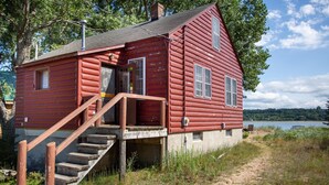 Une cabane en rondins rouge, avec un escalier en bois menant à une véranda, située au bord d’un lac.