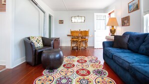 Un salon avec un canapé bleu, un fauteuil en cuir marron, une table à manger en bois avec des chaises et un tapis à motifs.