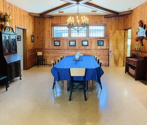 A dining area with a large table, wooden walls, and a chandelier.