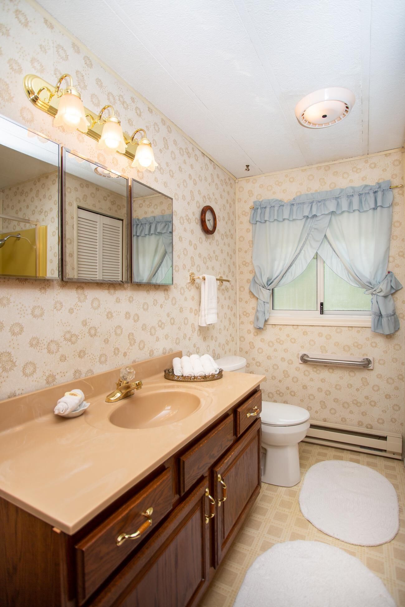 Un baño con tocador doble, inodoro, ventana con cortinas, perchero y barra de apoyo.