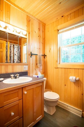 Ein Badezimmer in einer Holzhütte mit zwei Waschbecken, einer Toilette, einem Fenster und einem Spiegel.