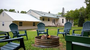 Une cabane rustique avec un foyer et des fauteuils Adirondack dans la cour.