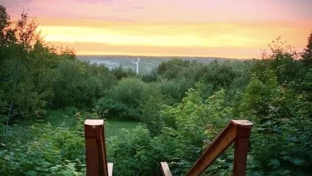 Eine Holzterrasse mit Blick auf einen Sonnenuntergang über einer bewaldeten Landschaft.