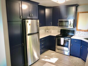 A modern kitchen with dark blue cabinets, stainless steel appliances, and a white countertop.