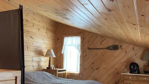 A cozy cabin bedroom with a bed, a chair, a desk, and a window.