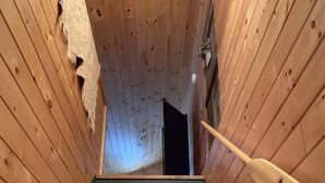 A wooden staircase with a dark floor leading upwards, flanked by wooden walls.